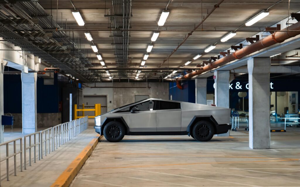 An electric Cybertruck is parked in a modern underground garage, showcasing futuristic automotive design.