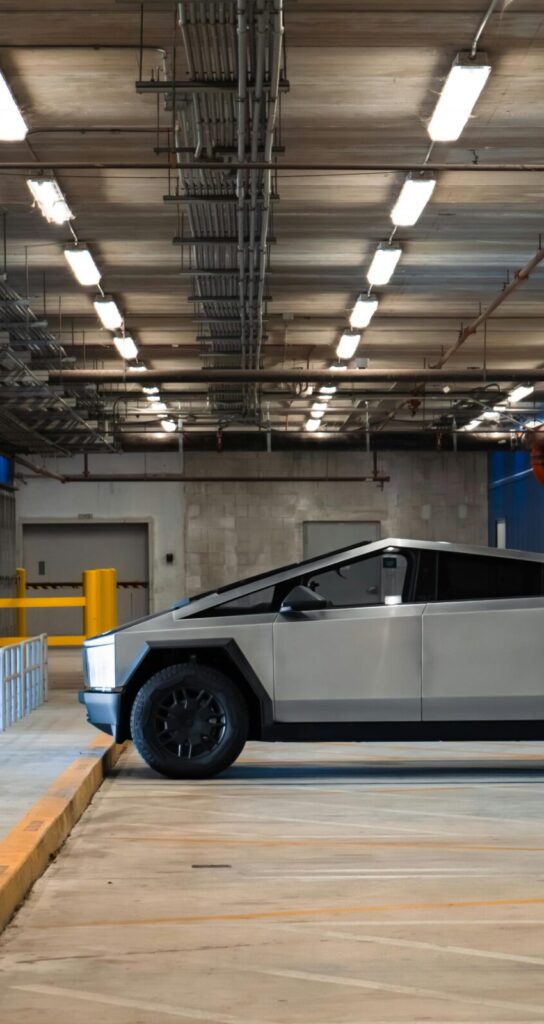 An electric Cybertruck is parked in a modern underground garage, showcasing futuristic automotive design.