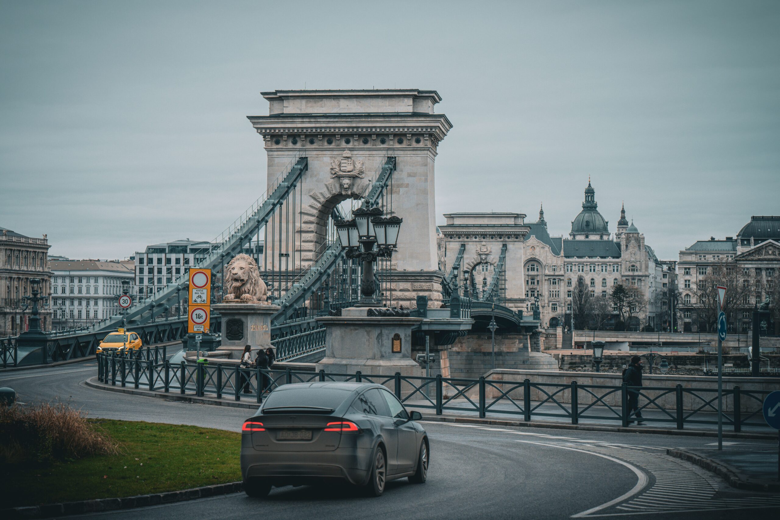 View of the iconic Chain Bridge in Budapest with a car in the foreground on a quiet day.