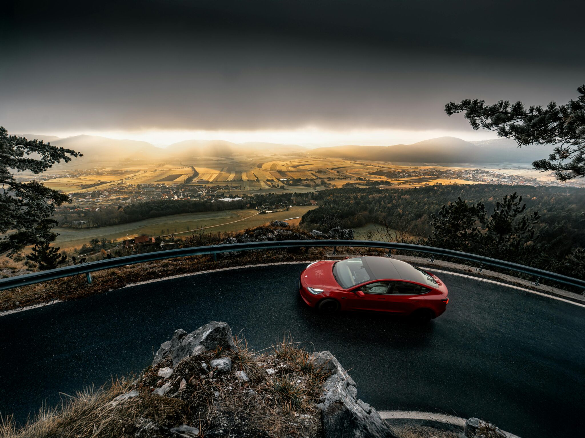 A striking red car navigates a winding road with a breathtaking view of Niederösterreich, Austria.