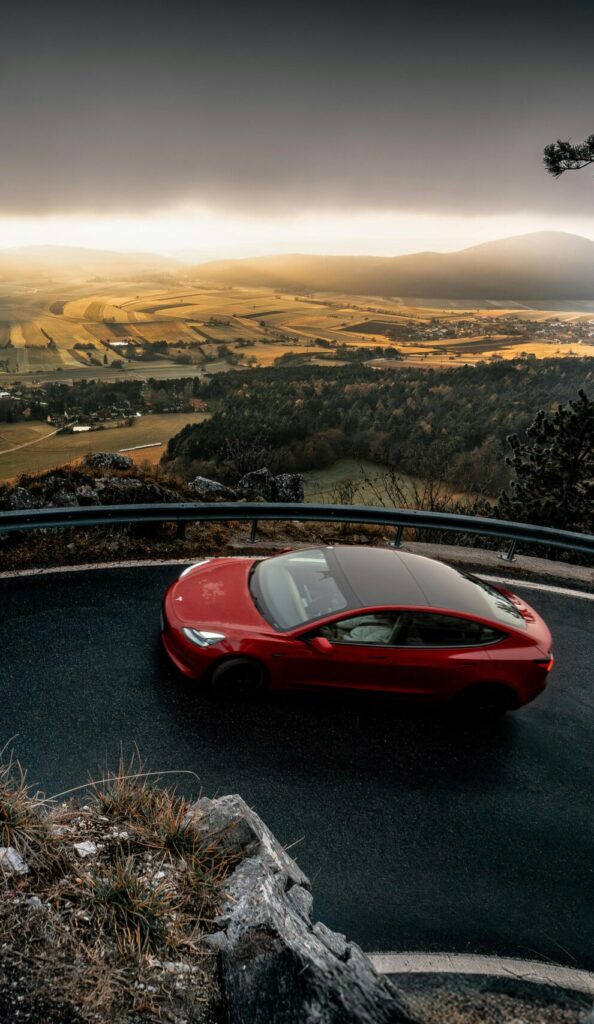 A striking red car navigates a winding road with a breathtaking view of Niederösterreich, Austria.
