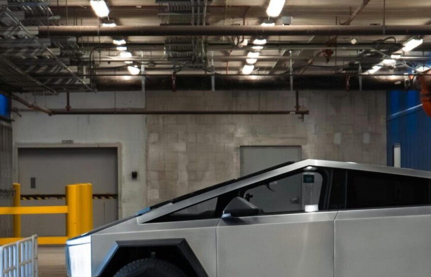 An electric Cybertruck is parked in a modern underground garage, showcasing futuristic automotive design.